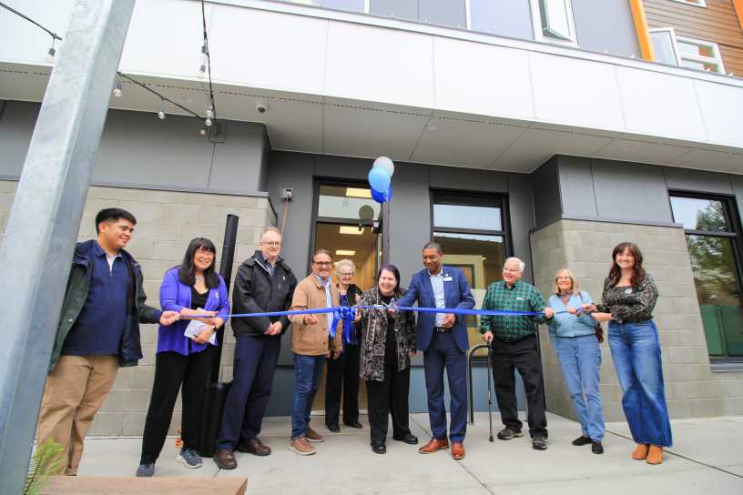 Ten people cutting a large blue ribbon.